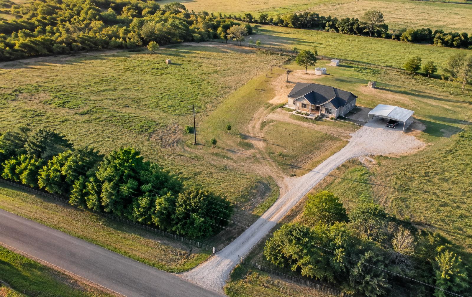 Aerial view of a land-home property with driveway and carport